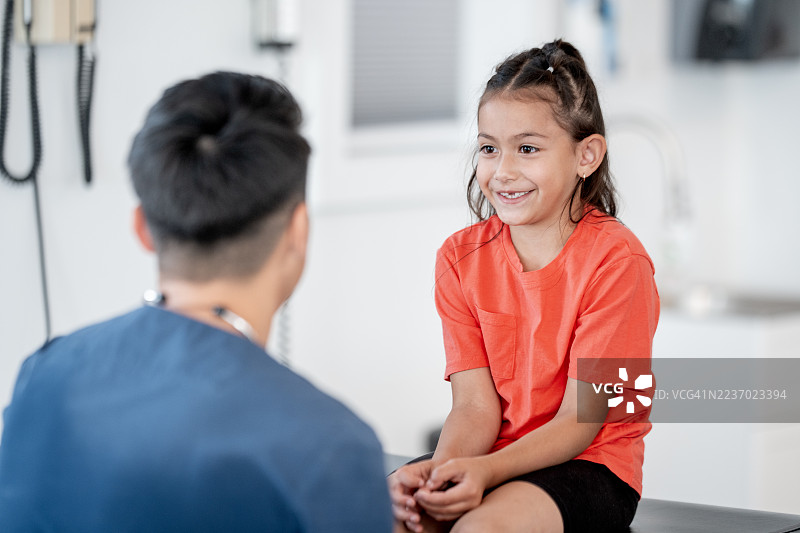 明亮诊所里医生为友好的拉丁裔小女孩进行体检，小患者就诊时面带微笑图片素材