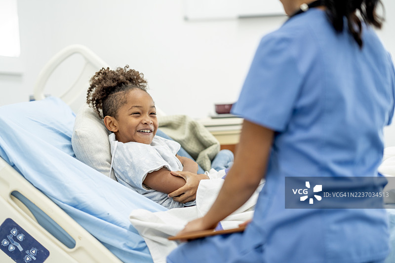 快乐的黑人儿童患者在现代病房的医院就诊时与护士一起大笑图片素材