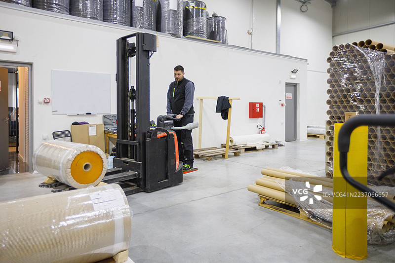工业设施中，仓库工人在大型卷筒和托盘之间操作叉车图片素材