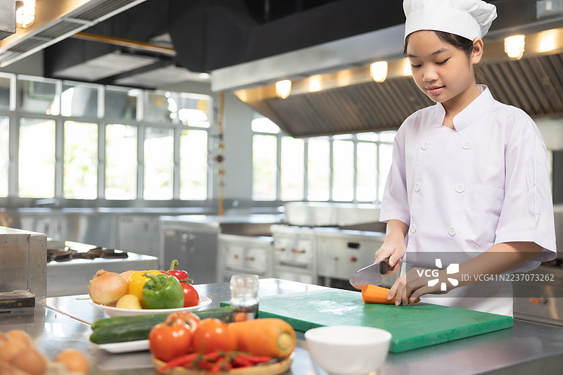 少女在食堂厨房做饭。老师和学生们在烹饪课上切菜。图片素材