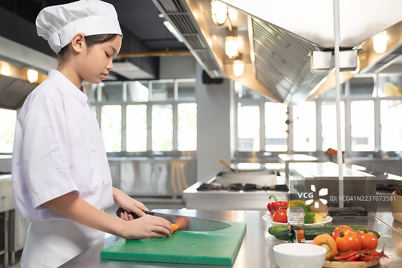 少女在食堂厨房做饭。老师和学生们在烹饪课上切菜。图片素材