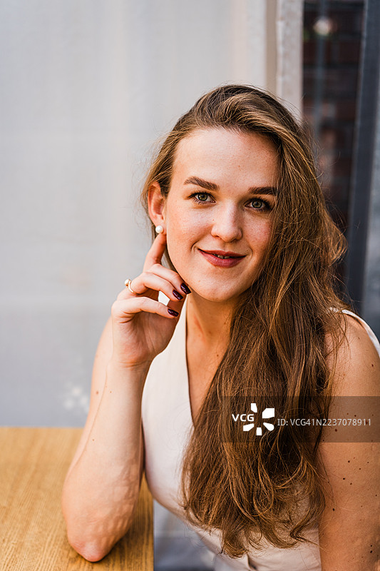 自信的女性坐在明亮自然光下的木桌旁图片素材