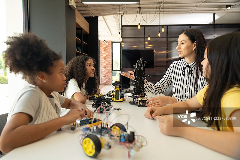聚焦机器人手臂，孩子们在老师的指导下进行动手STEM活动。多种族学生在机器人课程中与机器人车辆一起学习。图片素材