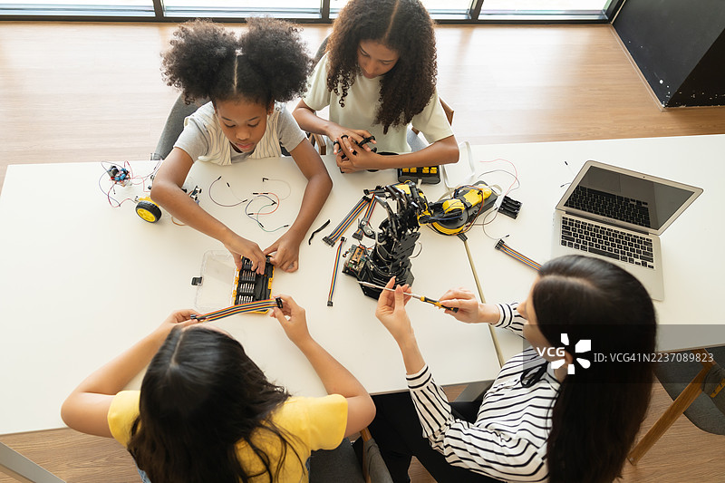 聚焦机器人手臂，孩子们在老师的指导下进行动手STEM活动。多种族学生在机器人课程中与机器人车辆一起学习。图片素材