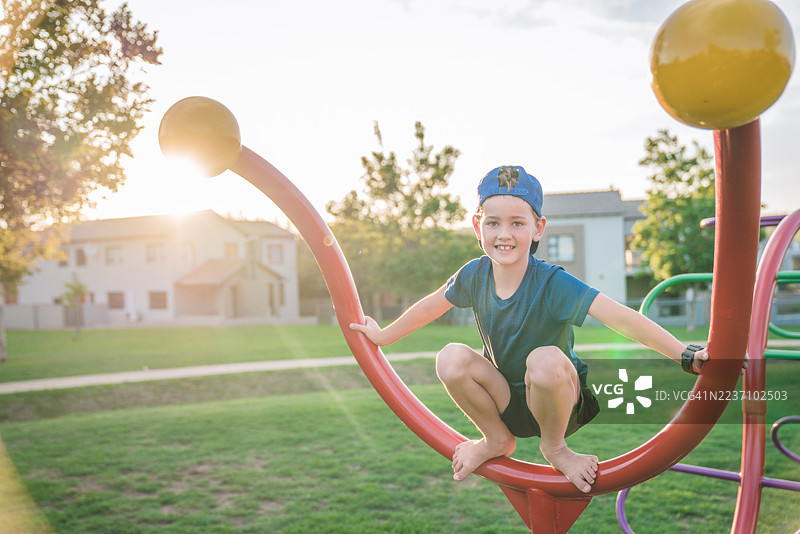 夕阳下，小男孩在公园游乐场快乐地攀爬图片素材