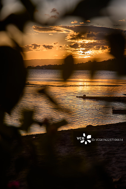 色彩斑斓的日落映照湖面，水面倒映着晚霞，背景是深邃的山丘。图片素材