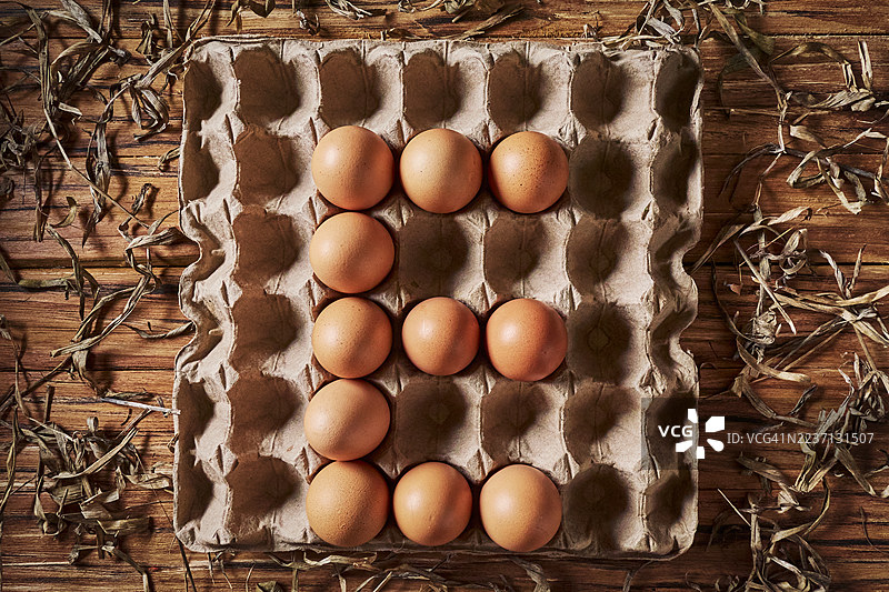 新鲜的棕色鸡蛋整齐地放在纸板蛋 carton 上，背景是质朴的木桌。图片素材