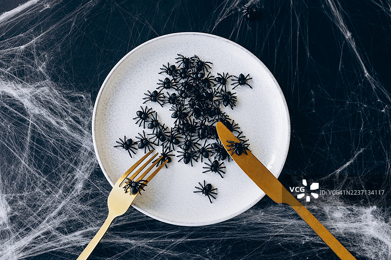 万圣节恐怖的桌面布置，盘子上有蜘蛛，黑色背景上的金色餐具图片素材