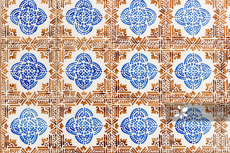葡萄牙复古蓝棕色阿祖莱霍瓷砖  描述：特写传统葡萄牙阿祖莱霍瓷砖，展示精美的蓝色花卉图案和几何棕色图案。磨损明显、边缘剥落的老旧表面突显了图片素材