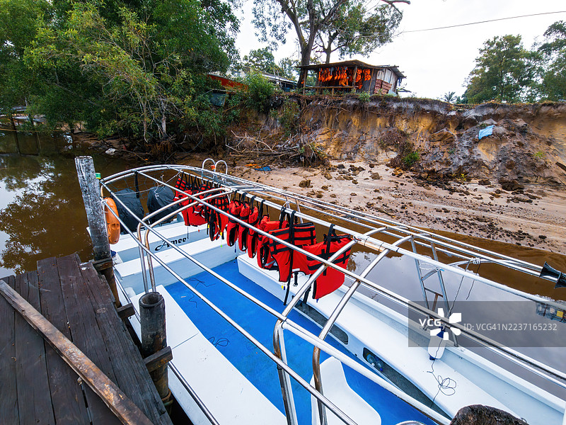 泥泞河岸边停靠的船只，配有救生衣，旁边是木制码头和郁郁葱葱的绿树，俯视角度拍摄。图片素材