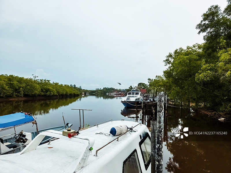 云层密布的天空下，宁静的湖泊上有船只，湖边绿意盎然，一派宁静的风景。图片素材