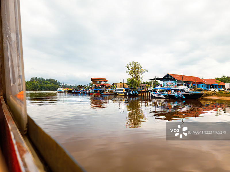 从行驶的船上看到的河景，河岸边停靠着建筑和船只，天空多云。图片素材