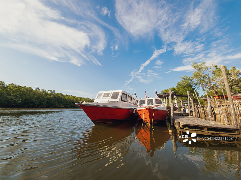 明亮的蓝天下，几朵薄云点缀其间，两艘小船停靠在河边质朴的木码头上。图片素材