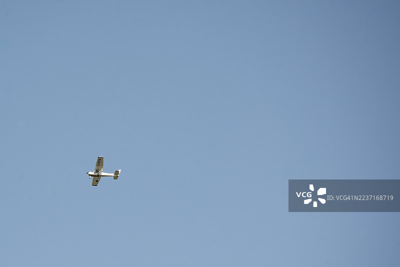 一架小型飞机在高远的晴朗蓝天中飞行，低角度仰视图片素材