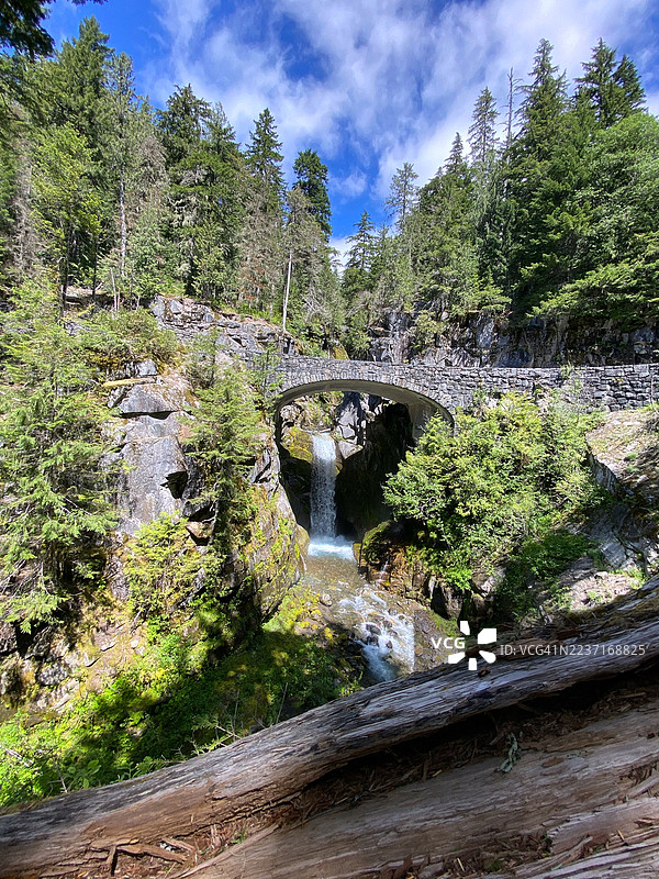 绿意盎然的森林中，一座石桥横跨奔腾的河流和瀑布，蓝天之下，阿什福德，美国，史蒂文斯峡谷路。图片素材