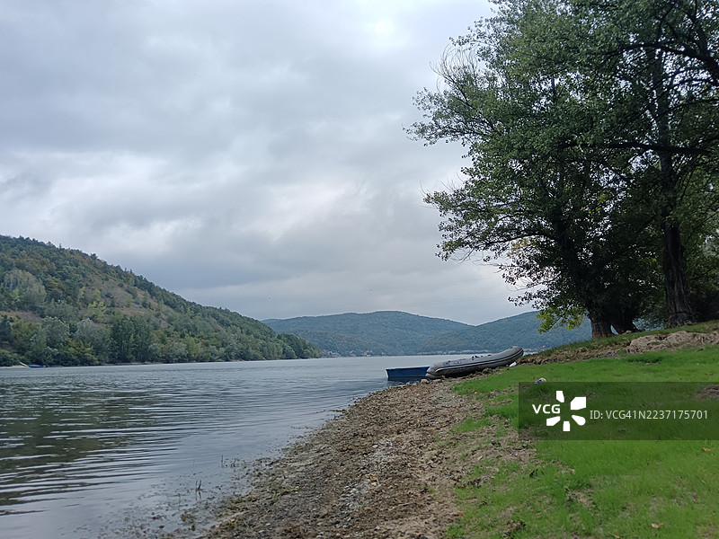 宁静的湖泊风景，有船只和青翠的山丘，天空多云。图片素材