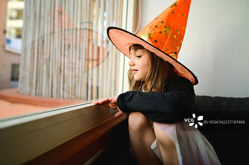 小女孩戴着巫师帽透过窗户看外面图片素材