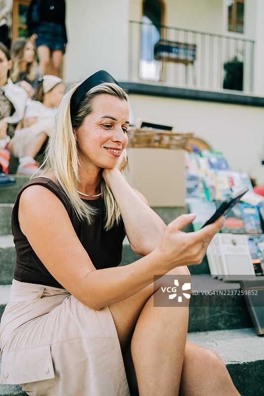 女人坐在户外书市的楼梯上，手里拿着手机。图片素材