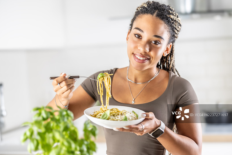 一位年轻的非裔美国女性正在享用她做的罗勒香蒜酱意大利面。图片素材