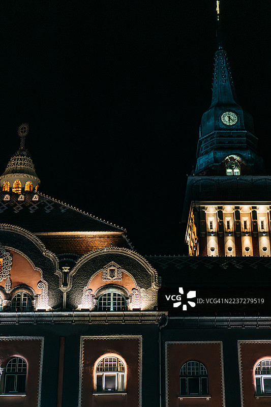 塞尔维亚苏博蒂察市的一座华丽市政厅在夜晚被灯光照亮，其拱形窗户闪烁着冷暖色调的光芒。图片素材