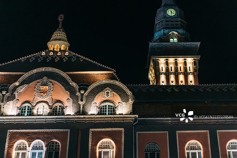 塞尔维亚苏博蒂察市一座华丽的市政厅在夜晚被照亮，其拱形窗户散发着温暖和凉爽的光芒。图片素材