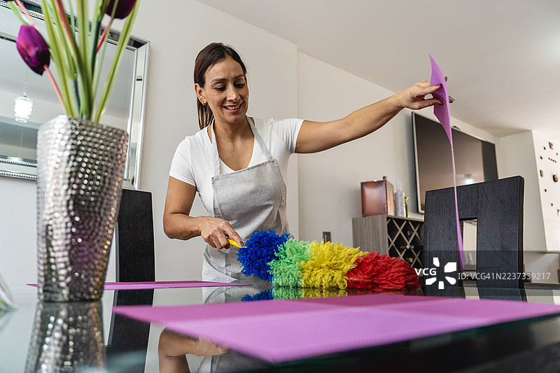 微笑的女性在家中为现代玻璃餐桌除尘。图片素材