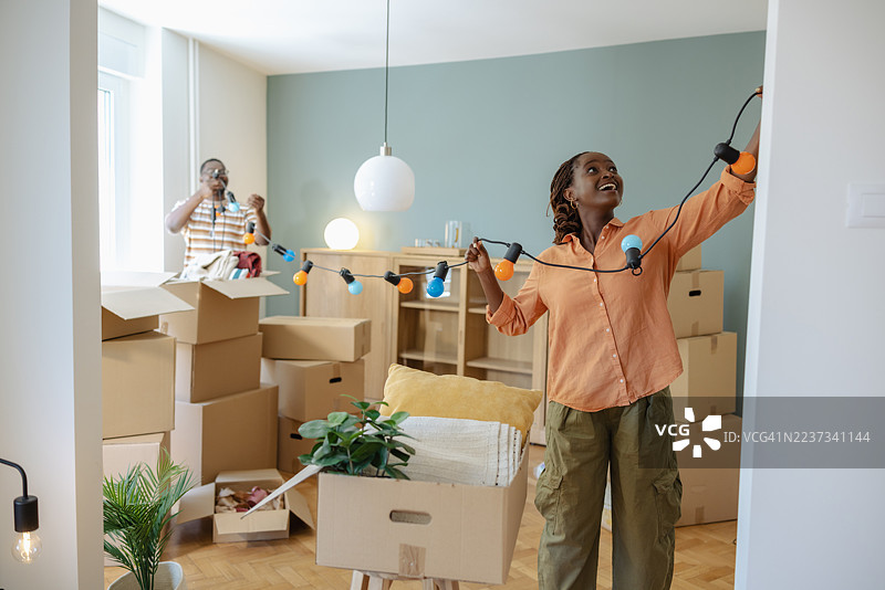 一对情侣在搬家时拆箱和装饰家，微笑着站在箱子和串灯之间图片素材