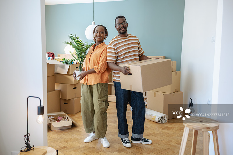 微笑的情侣搬进他们的新家，周围是打包箱。图片素材