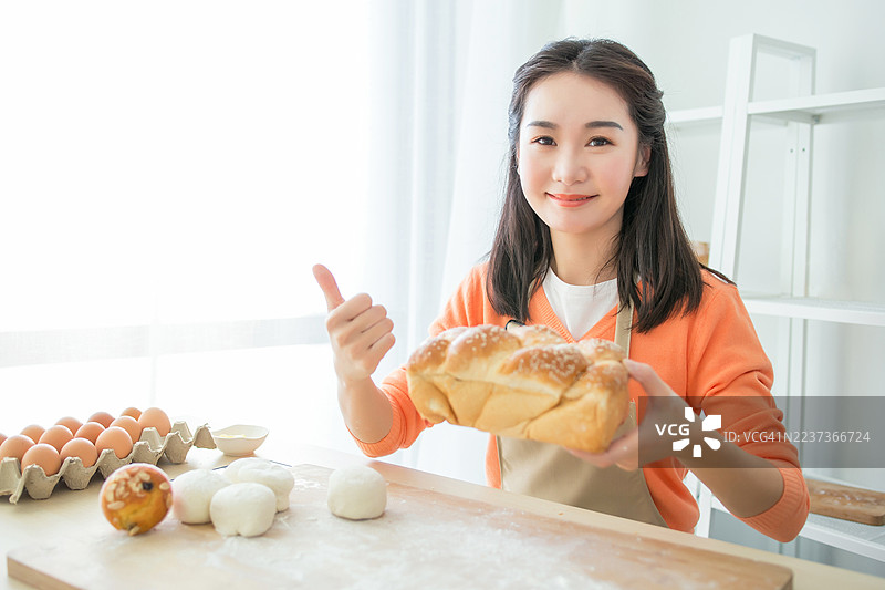 一位女性在明亮的厨房里展示刚出炉的面包。图片素材