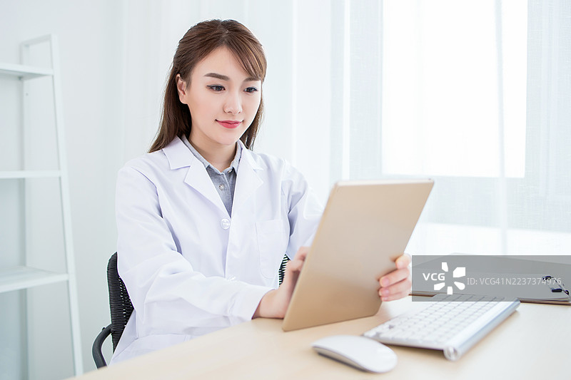 穿着白大褂的女医生在办公室的桌子上使用平板电脑图片素材