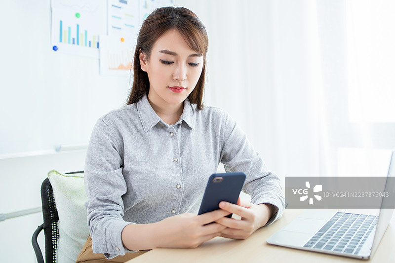 年轻女性在办公室使用手机和笔记本电脑图片素材