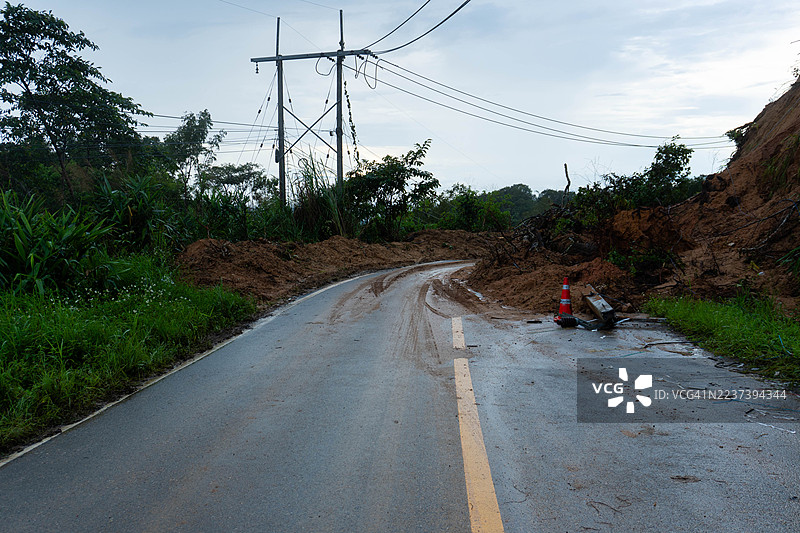 巨大的山体滑坡阻断了道路，泥土和碎石覆盖着沥青路面，上方有电线，还有一个交通锥警告危险。图片素材