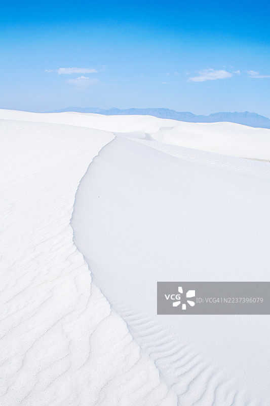 晴朗蓝天下白沙丘的风景，远处地平线上有山脉。图片素材