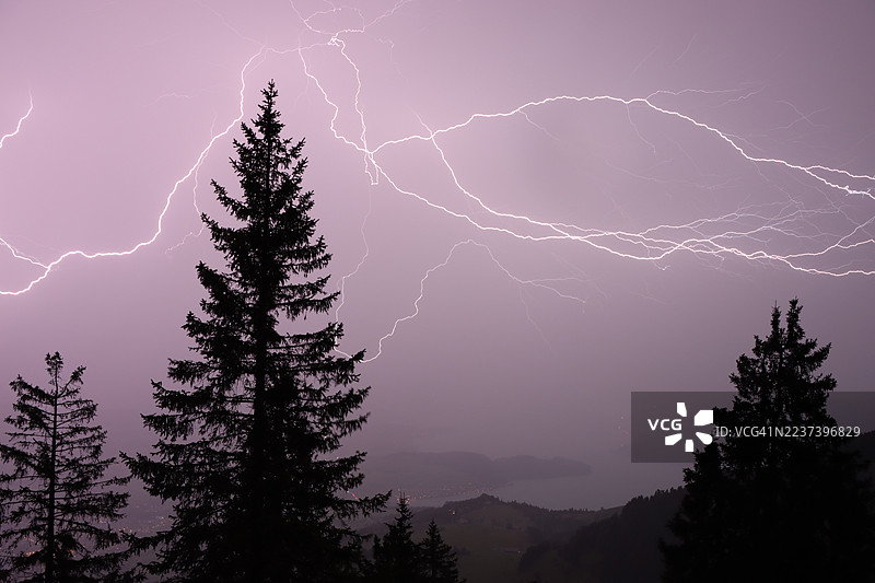 戏剧性的闪电照亮了夜空，树木和远处的湖泊在剪影中若隐若现。图片素材