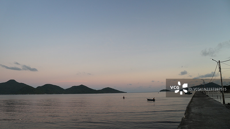 宁静的日落，平静的海面，远处的山峦，以及一艘载有小船的长码头图片素材