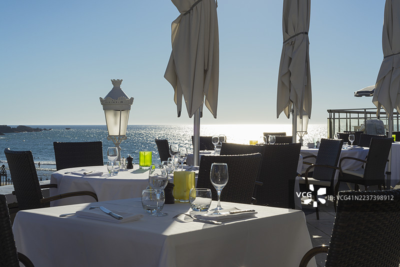 阳光明媚的一天，法国比亚里茨的户外餐厅露台上摆放着空桌椅，可俯瞰波光粼粼的大海，Biarritz,France图片素材