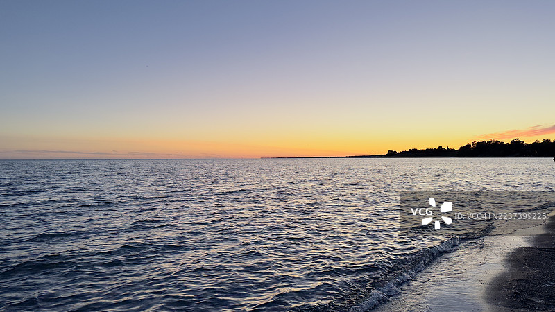 宁静的日落映衬着平静的海面和远处的海岸线图片素材