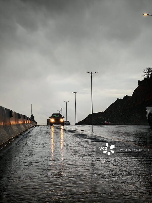 傍晚时分，雨天的道路上，车头灯倒映在湿漉漉的沥青路面上，沙特阿拉伯图片素材