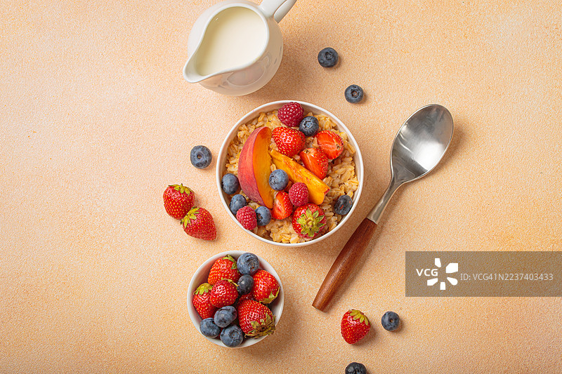 俯视一碗燕麦粥，配有新鲜浆果和桃子片，旁边放着牛奶和勺子，置于纹理表面上图片素材