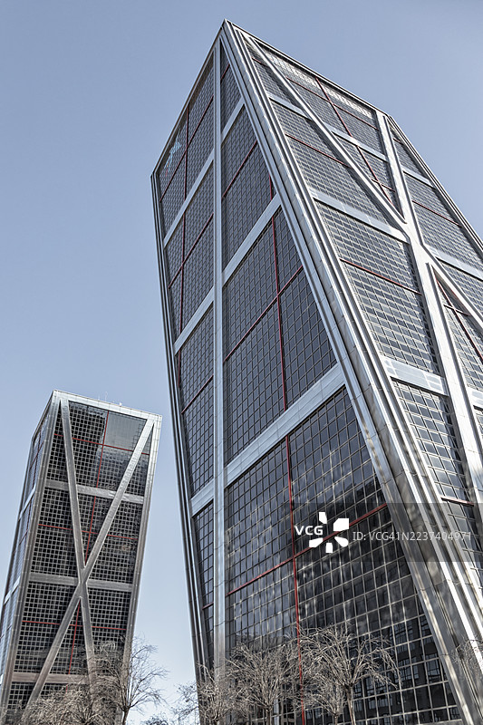 低角度拍摄的现代玻璃幕墙摩天大楼，背景是晴朗的蓝天，展示了当代建筑和城市发展，马德里，西班牙，拉巴斯图片素材