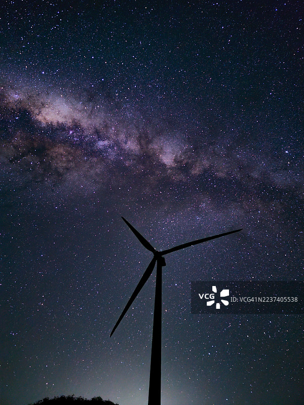 孤零零的风力涡轮机在令人惊叹的夜空中构成剪影，被璀璨的银河系照亮。图片素材