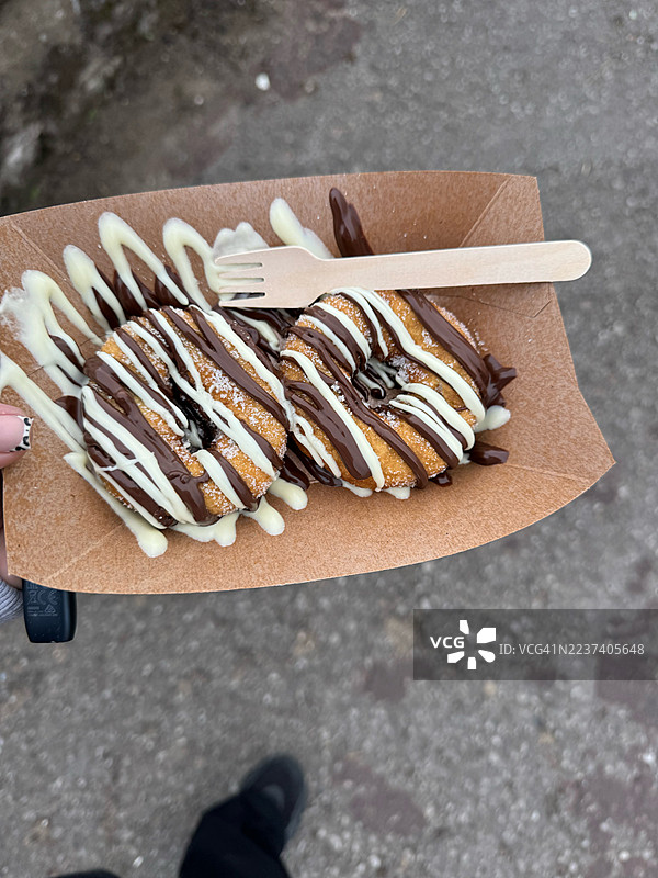 美味的西班牙油条，淋上巧克力和白巧克力酱，放在纸盘上。图片素材