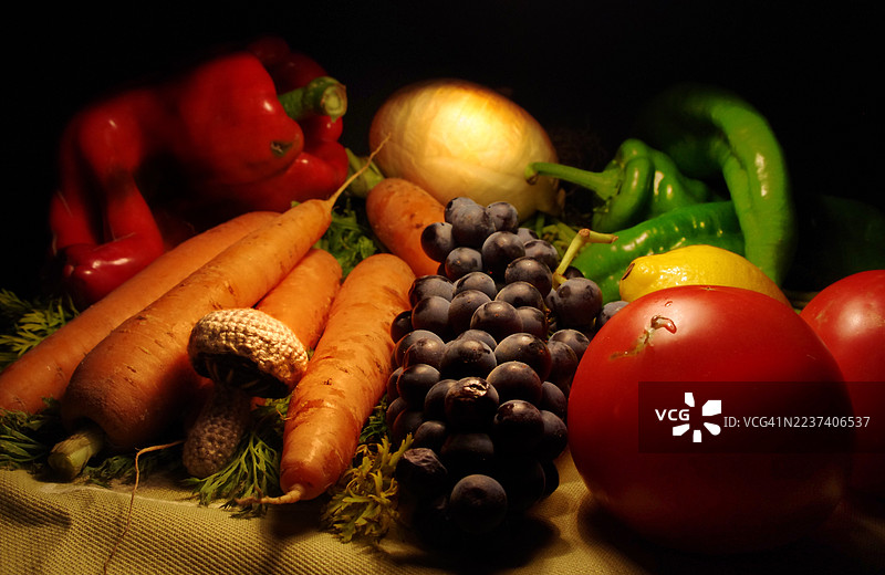 特写静物，桌上摆放着新鲜、色彩鲜艳的蔬菜和水果，光线戏剧化。图片素材