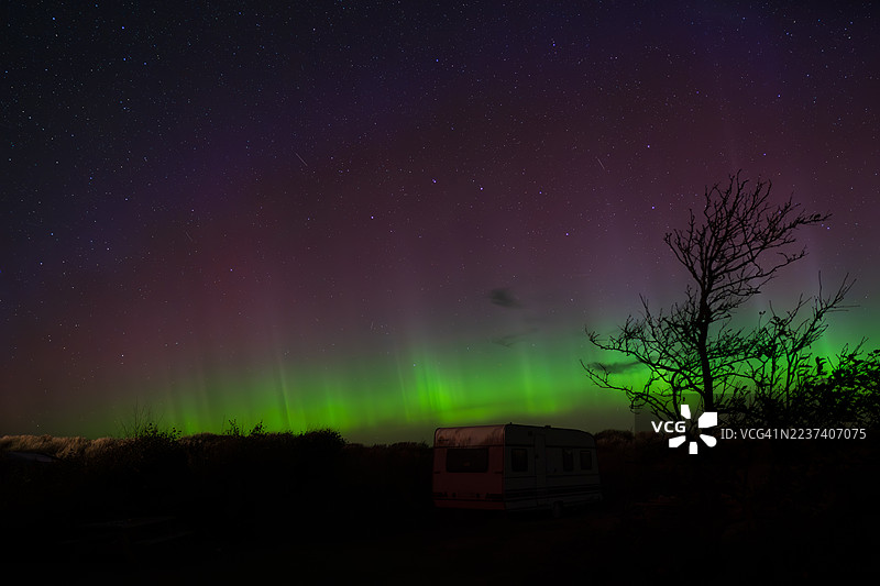壮观的北极光照亮了夜空，上方是一辆房车和剪影树木。图片素材