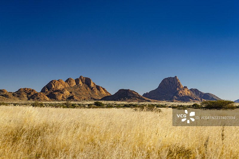非洲纳米比亚，金色草原绵延至古老的 the granite mountains，天空湛蓝而广阔。图片素材