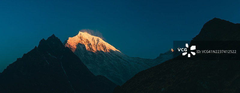 日出时分，在深邃的蓝色天空映衬下，雄伟的雪山之巅沐浴在金色光芒中，廓尔喀，尼泊尔，兰唐里隆（Langtang Lirung）图片素材