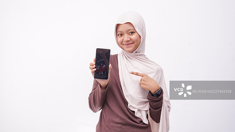 快乐的戴头巾的女孩，手中拿着一部展示空白屏幕的智能手机，背景为白色，孤立。图片素材