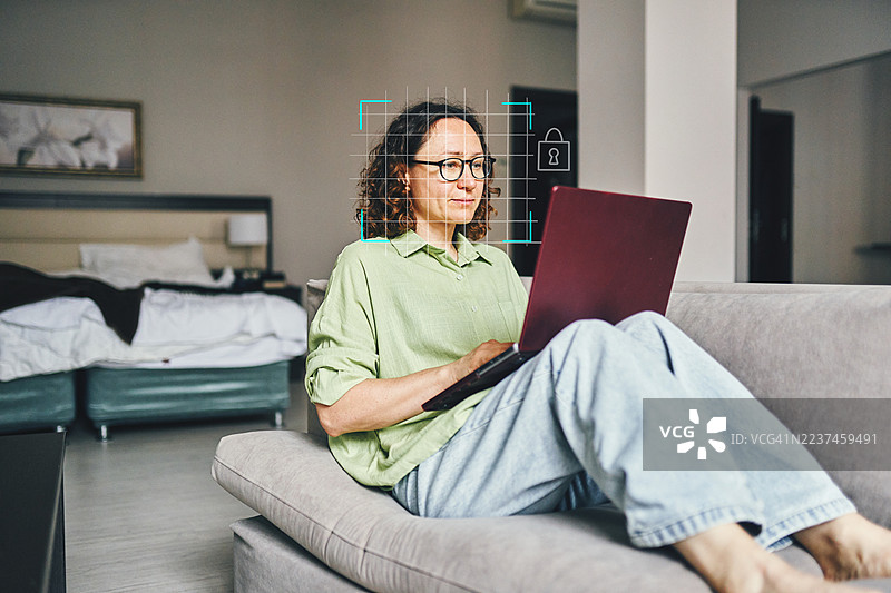 在现代客厅空间中，女性在沙发上使用笔记本电脑远程工作，带有安全覆盖层。图片素材