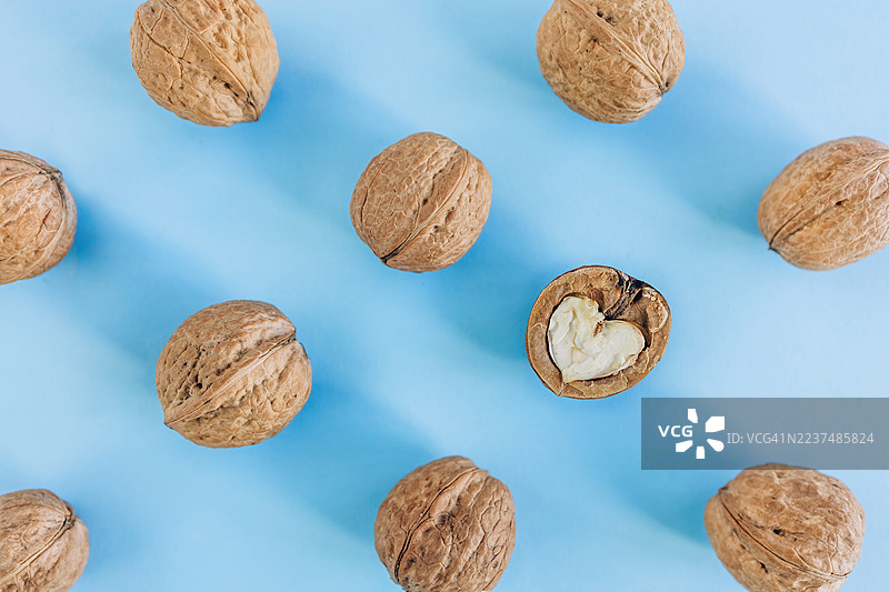蓝色背景上方视角的核桃，壳上有一个裂开的壳，露出心形的果仁。图片素材