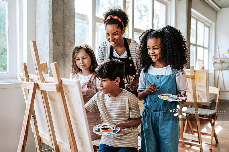 艺术老师与一群孩子在教室里欣赏学生的画作图片素材
